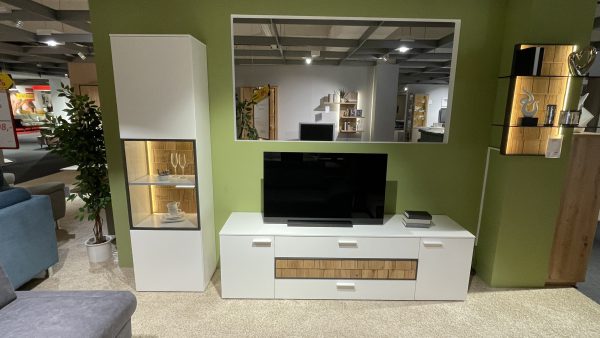 Das Wohnprogramm TV-Element in Weiß und Holz ist mit Regalen, Büchern und Dekoration ausgestattet und steht vor einer grünen Wand mit einem Spiegel darüber.