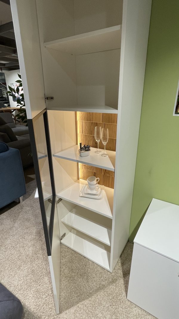 Wohnprogramm Weißer Eckschrank mit Glastür zeigt Gläser, Tassen und Untertassen an einer grünen Wand.