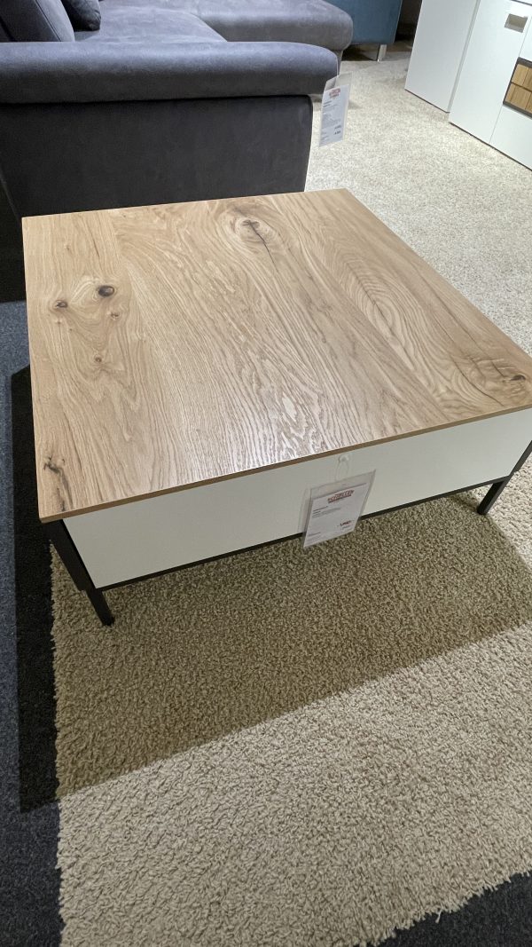 Couchtisch mit einer Platte aus hellem Holz, weißen Seiten und schwarzen Beinen auf einem beigen und dunkelgrauen Teppich.