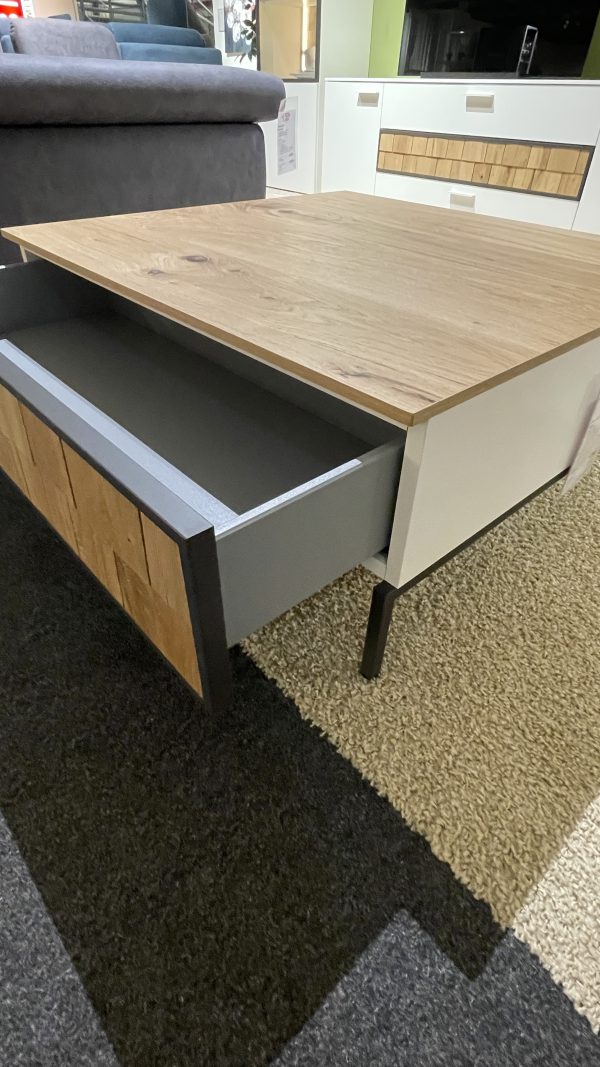 Ein Couchtisch mit einer teilweise geöffneten Schublade steht auf einem Teppichboden neben einem grauen Sofa.