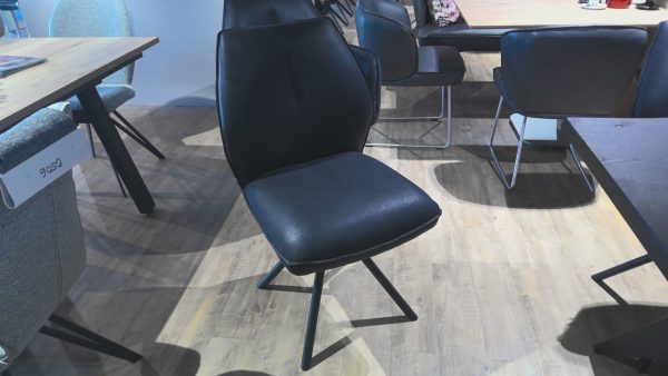 Die Esstischgruppe Interliving 5116, ein moderner schwarzer Stuhl mit Metallbeinen, steht auf einem hölzernen Ausstellungsraumboden.