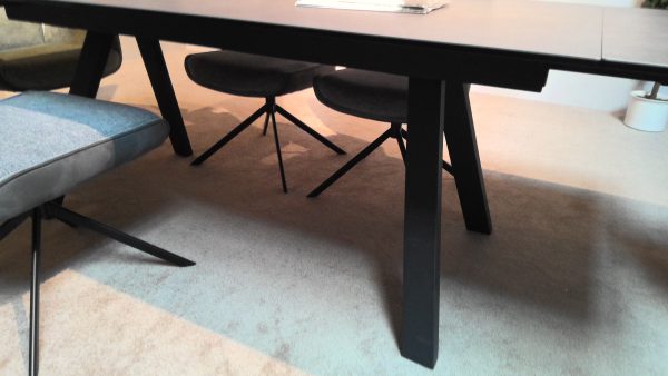 Tischgruppe Okinawa/Setubal: Schwarzer Tisch und Stühle mit abgewinkelten Beinen auf einem beigen Teppich in einem modernen Raum.