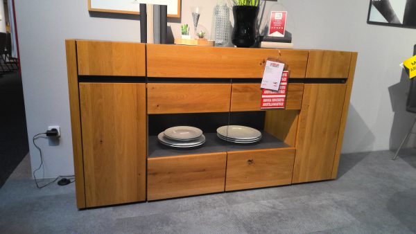 Anrichte Interliving-5603 Sideboard mit schwarzen Akzenten, Tellern auf dem Regal und einem Verkaufsschild, das davor hängt.