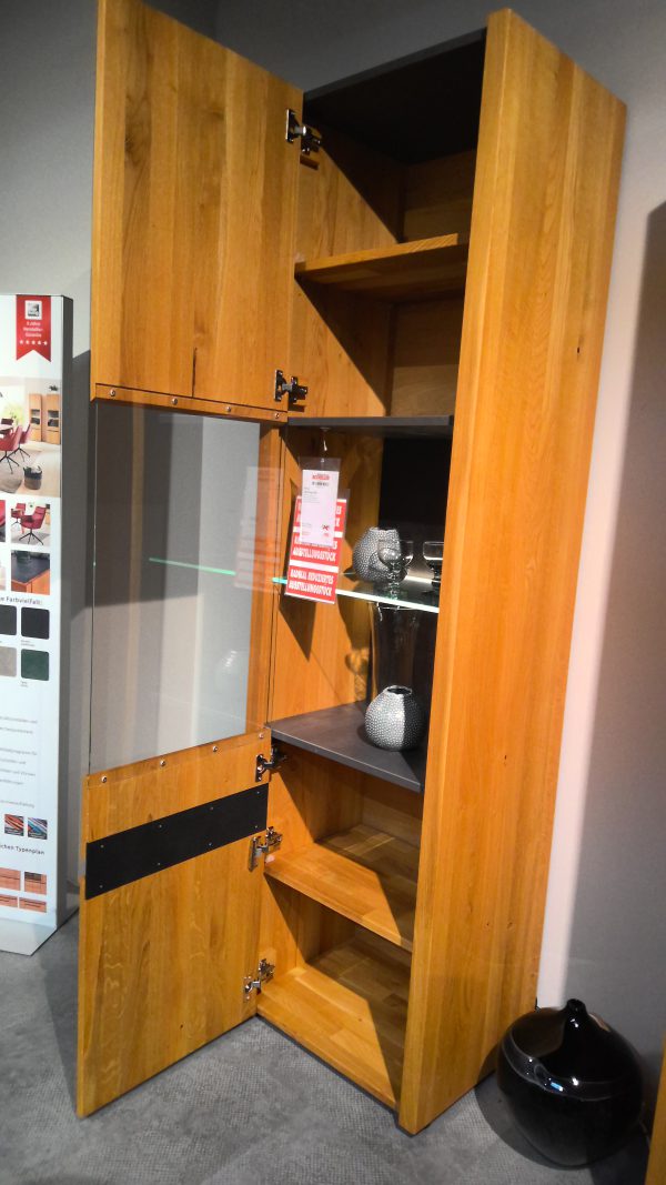 Die Anrichte Interliving-5603 ist eine hohe Holzvitrine mit einer Glastür, die Regale mit Dekorationsartikeln offenbart.