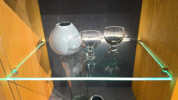 Eine runde, strukturierte Vase und zwei Glaspokale stehen auf dem Glasregal Anrichte Interliving-5603 mit Holzseiten.