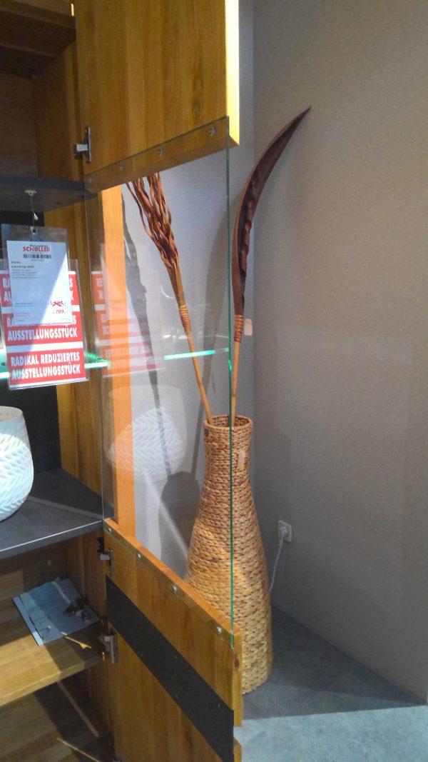 Eine hohe Korbvase mit getrockneten Pflanzen steht hinter der Glastür eines Vitrine Interliving-5603 Schranks.